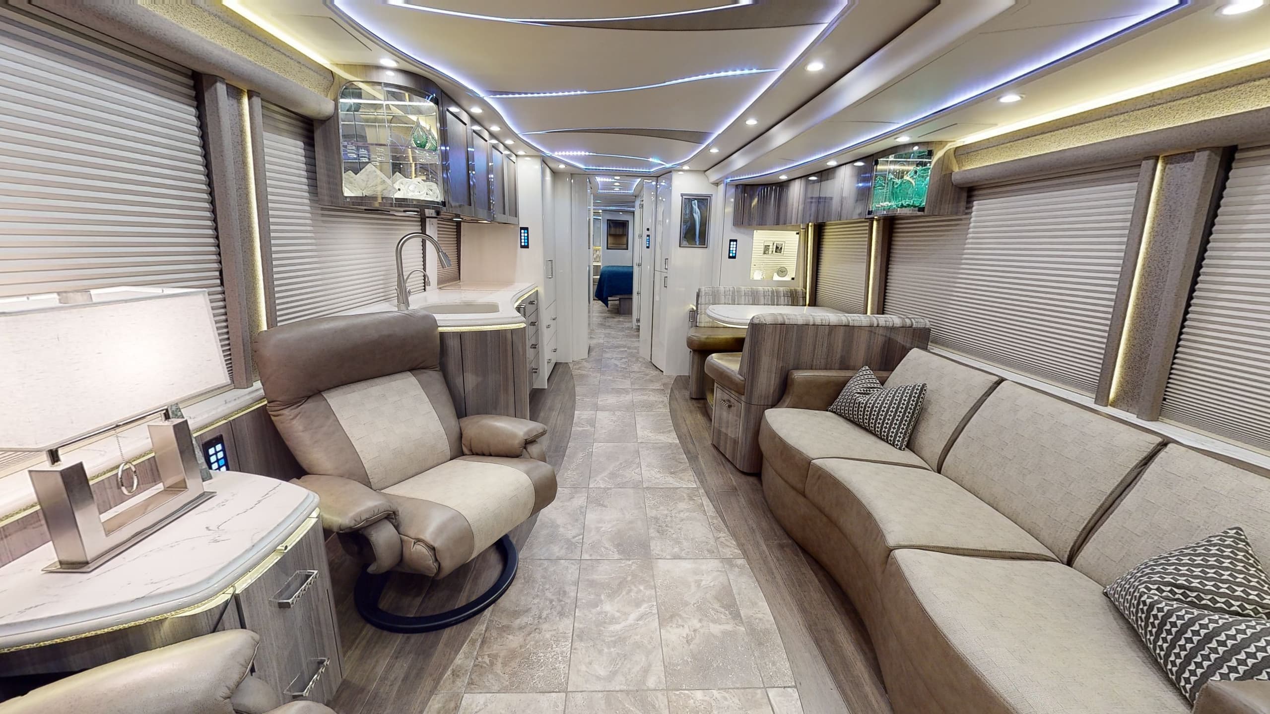 Interior of a luxury RV with white and blue accent lighting and comfortable seating.