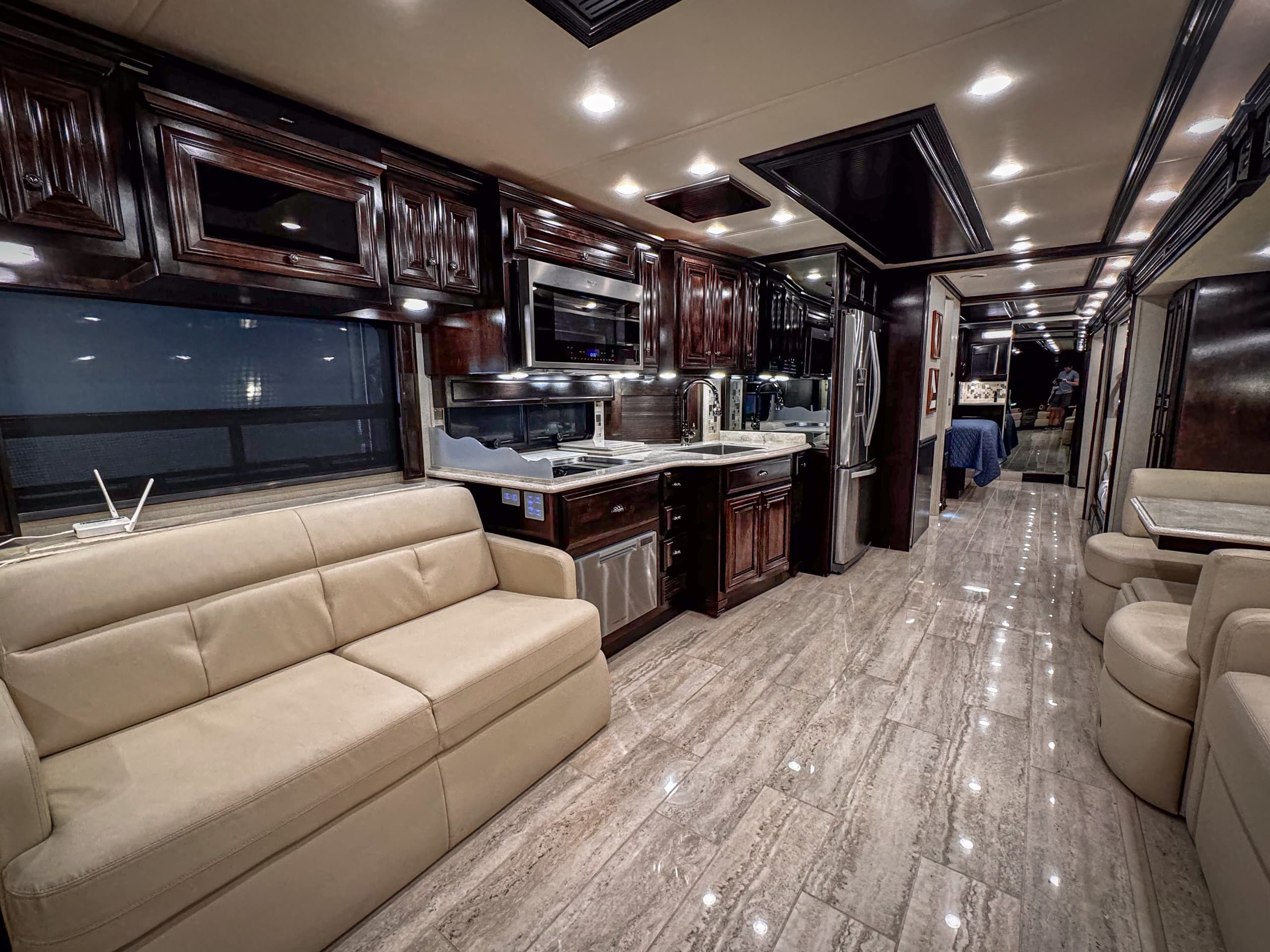 Interior of a luxury RV with stainless steel appliances and dark wood cabinets.